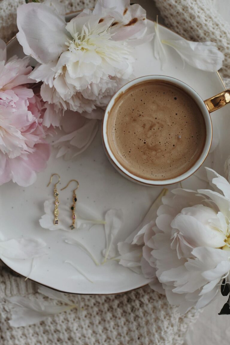 A beautifully arranged flat lay with coffee, peonies, and earrings on a white plate.