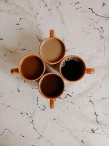 Four brown mugs of coffee on a marble surface viewed from above.